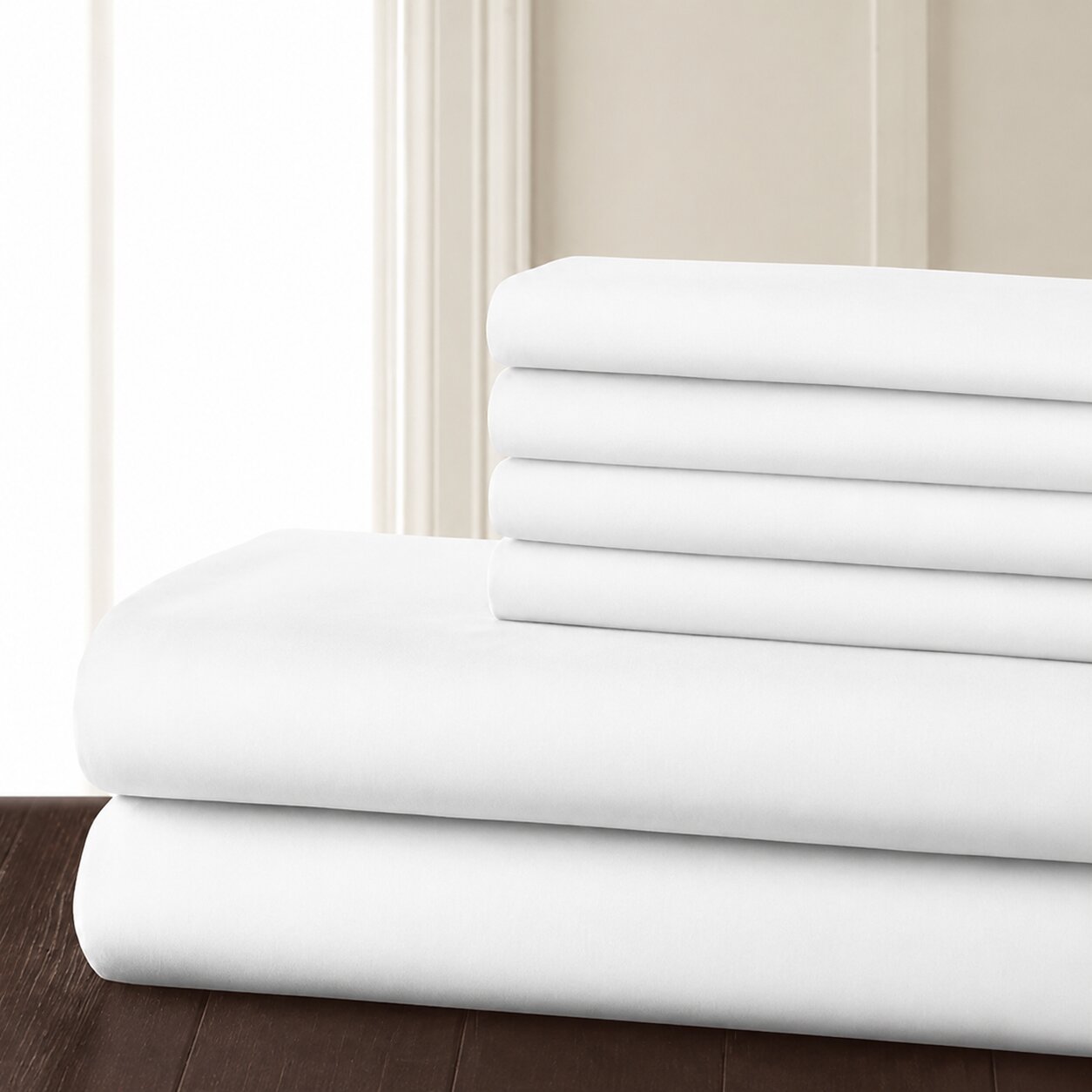 White hotel bed sheet set neatly folded on wooden surface, solid white bedding for hospitality guest rooms.